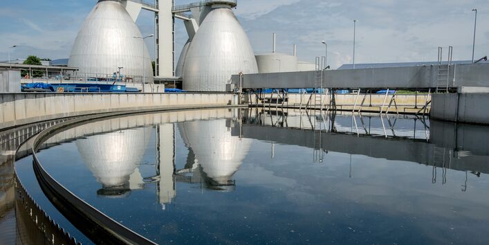 Foto von Faultürmen, die sich im Nachklärbecken einer Kläranlage spiegeln