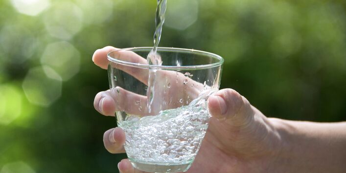 Eine Hand hält ein Glas unter einen Wasserhahn