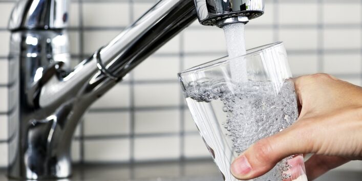Ein Glas wird unter einem Wasserhahn gefüllt.