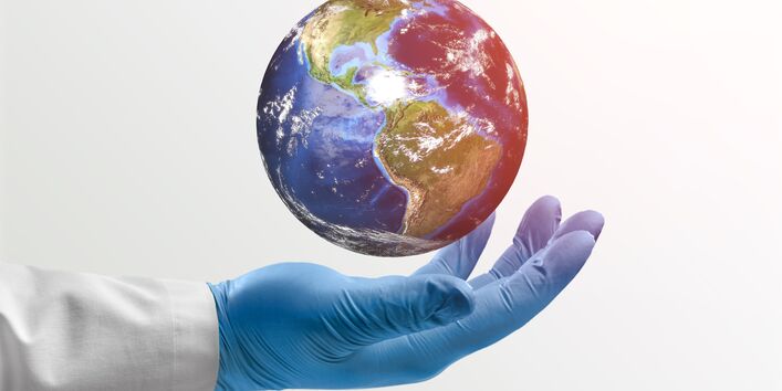 Photo of an arm with a doctor's coat and gloves holding a globe.