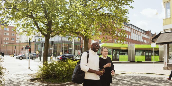 Zwei Menschen laufen lächelnd durch das Bild. Im Hintergrund eine grüne Straßenbahn.