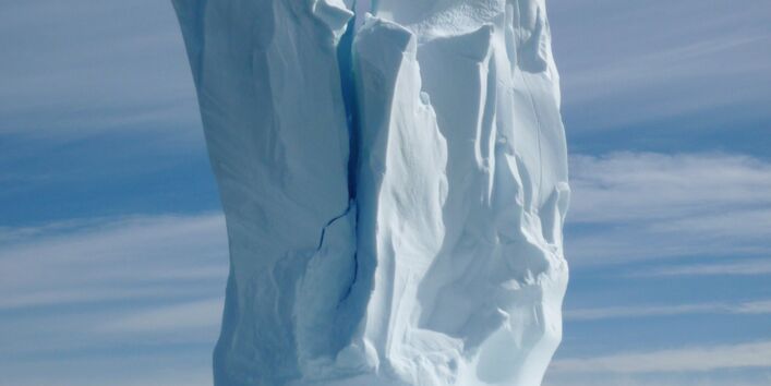 Auf dem Meer schwimmt ein Eisberg. Er sieht aus wie eine Skultpur. Unten eine breite Fläche auf der die Figur sitzt. von oben geht ein spalt durch die Figur bis etwa zur Hälfte. 