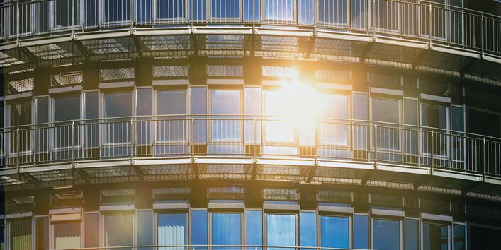 The picture shows the glass frontage of a house reflecting the sun. Some of the windows are part-shaded by means of external roller shutters.