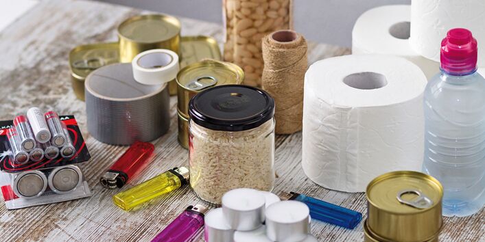 The picture shows an assortment of emergency provisions including groceries such as beans, rice and tinned food, batteries, adhesive tape, toilet paper, tea lights and lighters. 