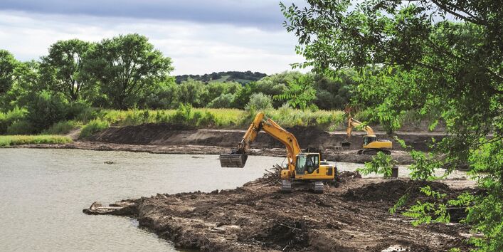 The picture shows a water body on the edge of which a construction measure is being carried out. The edge of the bank is open ground where two dredgers are active.