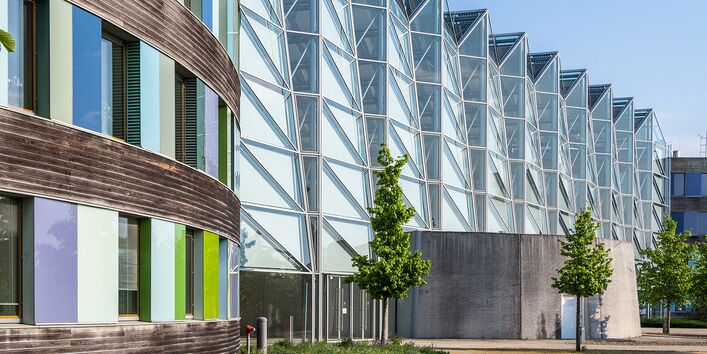 Zu sehen ist das Hauptgeäude des Umweltbundesamtes in Dessau-Roßlau. Im Anschtt befindet sich ein Teil der bunten Fassade sowie die Blickrichtiung zum gläsernen Haupteingang. 