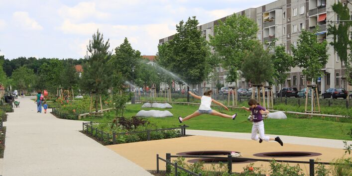 Ein Foto auf dem Mehrfamilienhäuser zu sehen sind mit einer Park- und Grünfläche davor. 