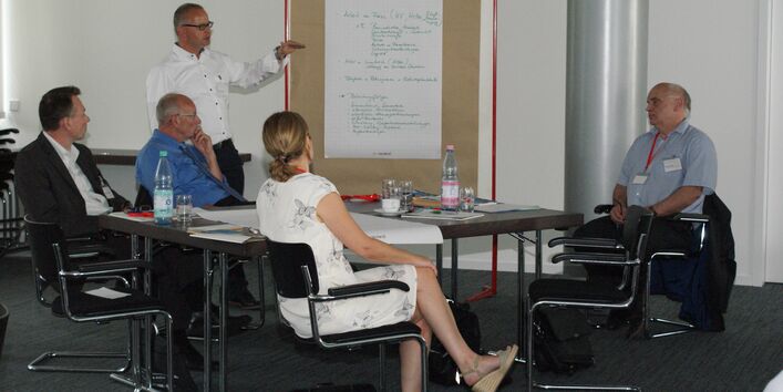 Vortragender steht an einer Moderationswand und erläutert die Arbeitsgruppenergebnisse, die dort handschriftlich angepinnt hängen.