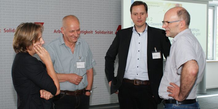 Vier Teilnehmer stehen diskutierend zusammen und schauen freundlich zueinander.