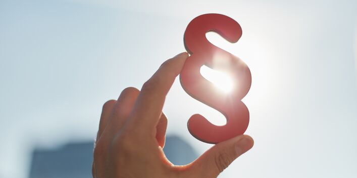 ParagrafenSymbol wird in der Hand halten, vor einem Himmel. Es scheint die Sonne. 