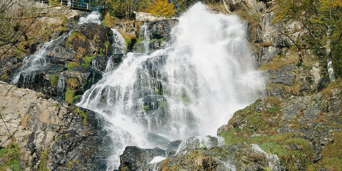 Wasserfall von einem großen Felsen mit vielen Bäumen im Hintergrund