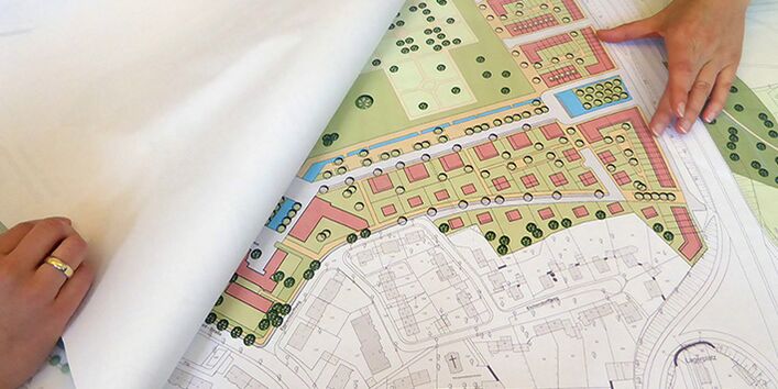 Die Rahmenplanung liegt aufgeschlagen vor. Zwei Hände halten das Papier aufgeschlagen und zeigend auf die farbige Projektskizze.