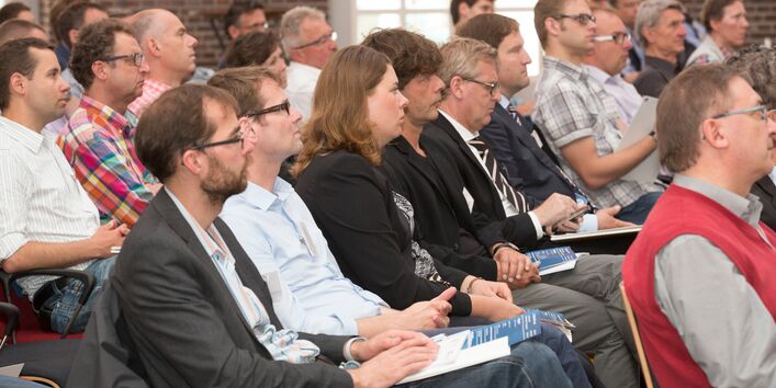 Personen sitzen im Publikum und hören aufmerksam zu