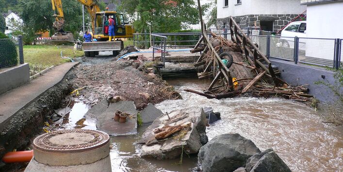 Die Sturzflut riss Straßen auf und spülte Brücken fort. Im Hintergrund befinden sich Helfer auf einem Bagger.