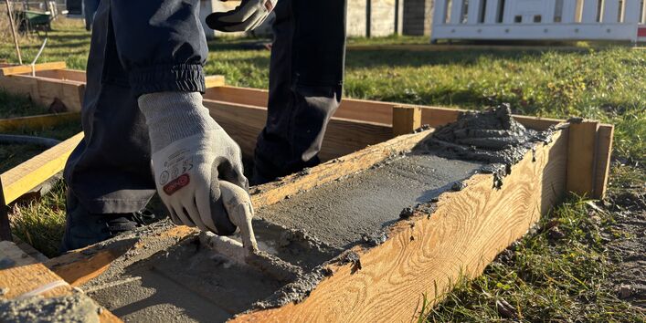 Das Bild zeigt einen Schüler, wie er den bereits gegossenen und verdichteten Beton mit einer Kelle glättet.