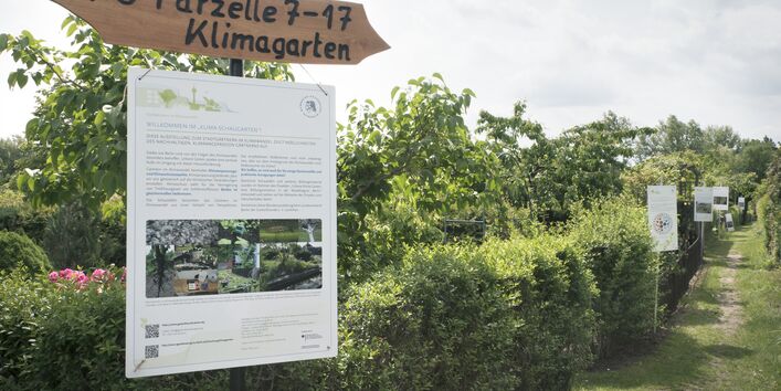 Fotografie eines Wegweisers der Parzelle Klimagarten. Am Wegweiser befindet sich zudem eine Informationstafel zum "Klima-Schaugarten".