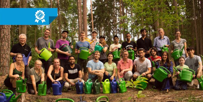 Gruppenbild von Freiwilligen bei der ersten Gießaktion. Die abgebildeten Personen halten Gießkannen in den Händen. Sie stehen im Wald.
