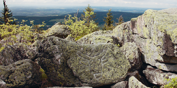 Aufgeschichtetes Felsengestein auf dem Ochsenkopf gibt einen Blick frei über das Fichtelgebirge. In der Ferne ist der Horizont sichtbar.