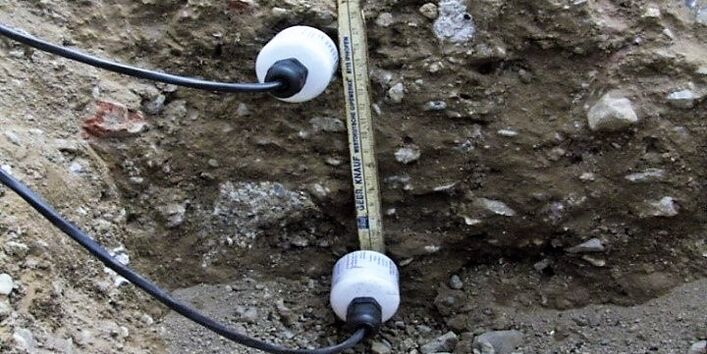 Ein Temperaturmessgerät in Röhrchenform liegt auf einen Bodenquerschnitt. Die weißrunden Tempertaturfühler liegen ebenfalls auf dem Bodenquerschnitt