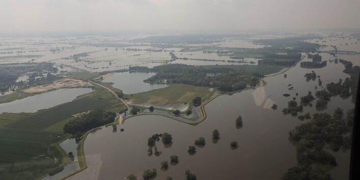 Luftaufnahme von einem überschwemmten Gebiet nach einem Deichbruch. Aus dem Wasser ragen an einigen Stellen Baumwipfel.