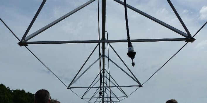 Exkursionsteilnehmende stehen zuhörend an einer Beregnungsanlage unter deren Gestänge im Freien.