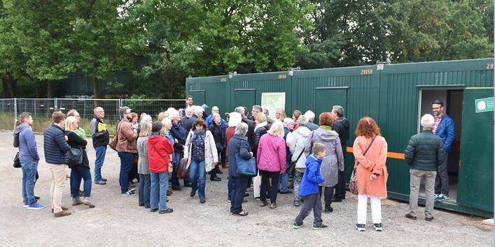 mehrere Personen versammeln sich vor Containern, um an einer Geländeführung teilzunehmen