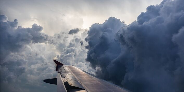 Fotografie eines Flügels eines Flugzeugs im Flug. Der umgebende Himmel ist voller dunkler Wolken.