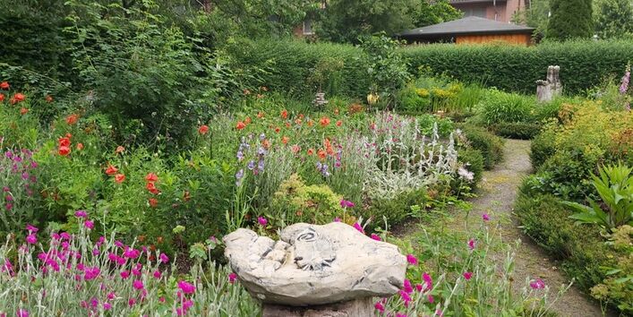 In einem Garten mit bunten Blumen steht eine Steinskulptur.