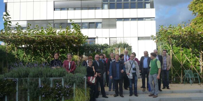 Männer und Frauen stehen in der Gruppe auf einer Treppe vor einem weißen kastenförmigen Gebäude mit Fenstern.