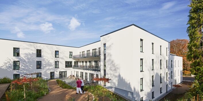 Fotografie eines Gebäudes, das von einer grünen Parkanlage umgeben ist.