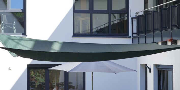 Fotografie eines Sonnensegels, dass über einer außen liegenden Aufenthaltsfläche gespannt ist.