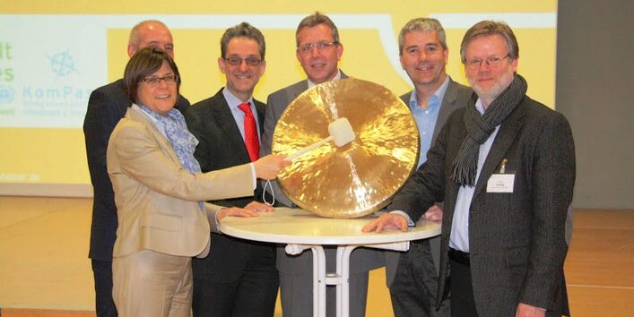 6 Personen stehen an einem Tisch und schlagen einen Gong.