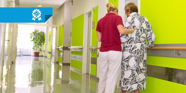 Eine Pflegekraft unterstützt eine Patientin beim Laufen.