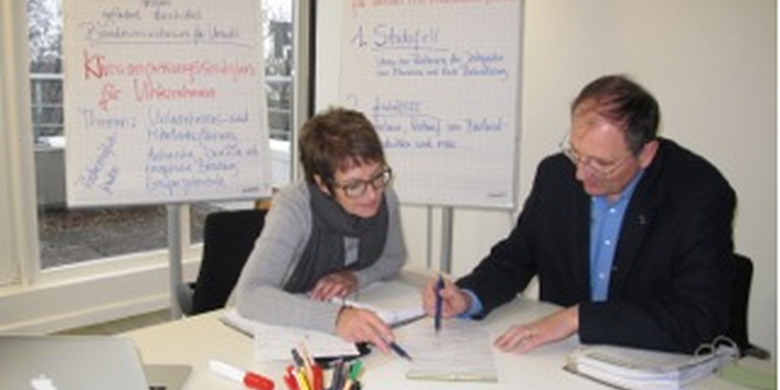 Zwei Personen sitzen am Tisch und arbeiten am Thema Klimaschutz und Anpassung an den Klimawandel