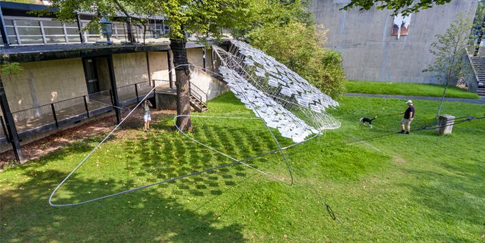 Drohnenaufnahme der aufgebauten Solar Spline-Konstruktion. Auf dem Boden wirft die Konstruktion Schatten. Die Photovoltaik-Module reflektieren Sonnenlicht.