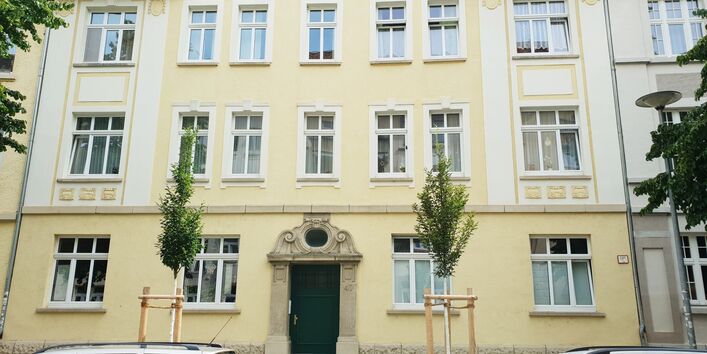 Fotografie eines Gebäudes, vor dem zwei Bäume neu angepflanzt wurden.