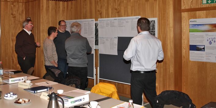 Mehrere Personen stehen vor zwei Pinnwänden auf denen Listen angepinnt sind.