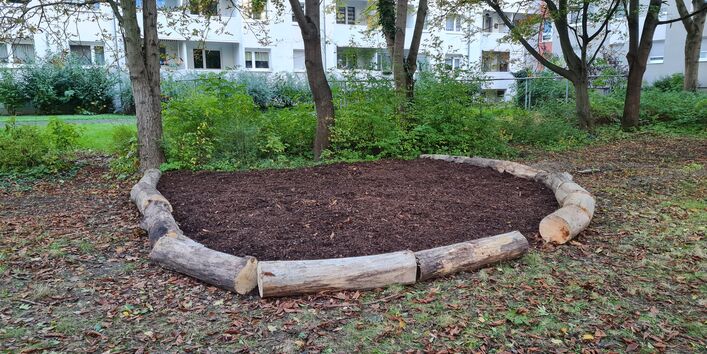 Zu sehen ist eine halbmondförmige Sitzecke, die mit Mulch ausgefüllt und von Baumstämmen umrandet ist.