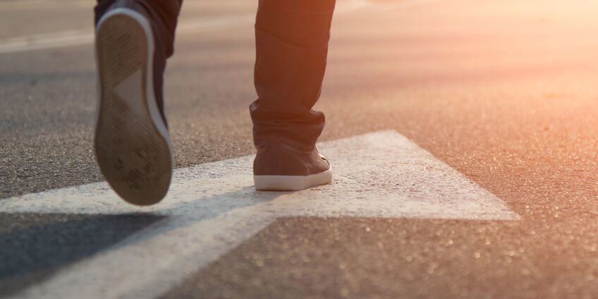 Ein Fußgänger läuft über einen Pfeil in den Sonnenuntergang