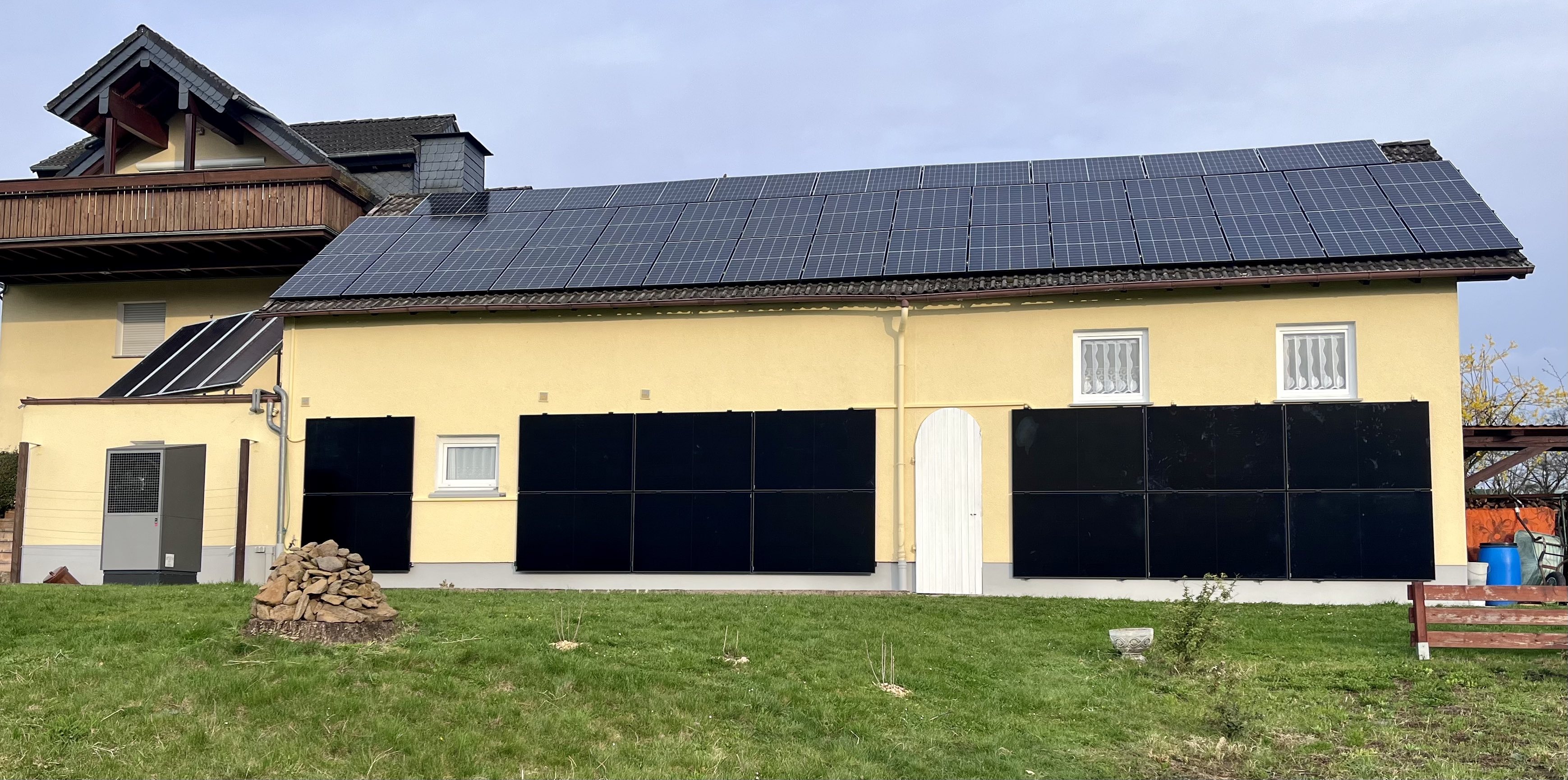 Außenansicht eines Gebäudes auf einer Wiese vor blauem Himmel, inkl Solarthermie und Photovoltaik auf dem Dach