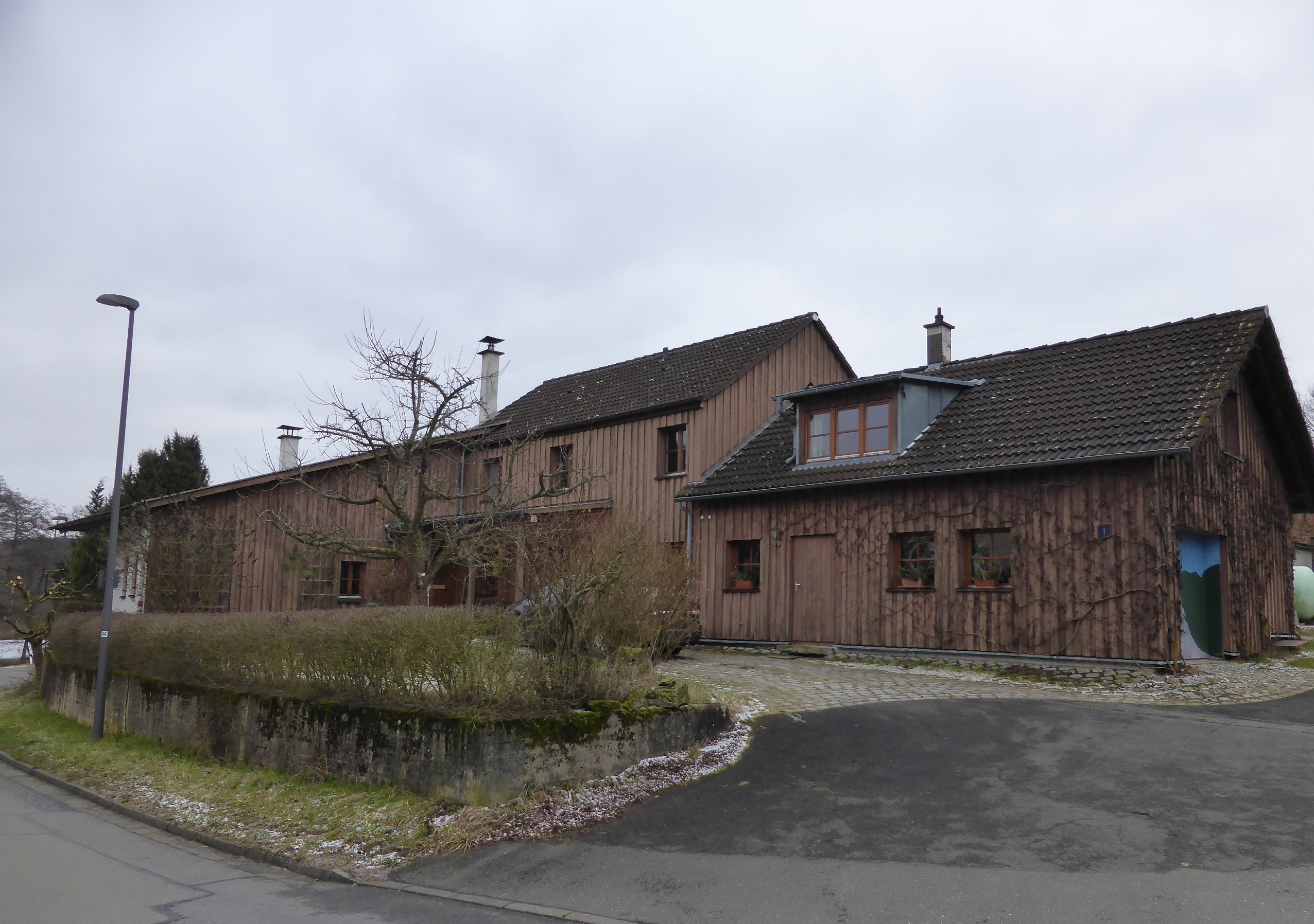 Ein langgestrecktes, holzverkleidetes Gebäude aus mehreren Teilen, Straßenansicht.