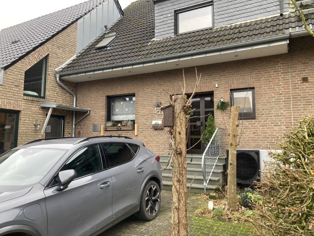 Ein Wohngebäude mit Wärmepumpe, davor ist ein Auto geparkt.