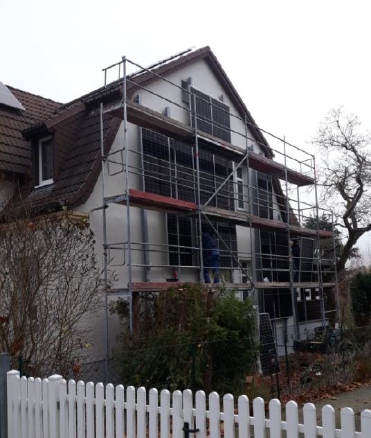 Eine Gebäudefassade, bedeckt mit PV-Modulen, davor steht ein Baugerüst.