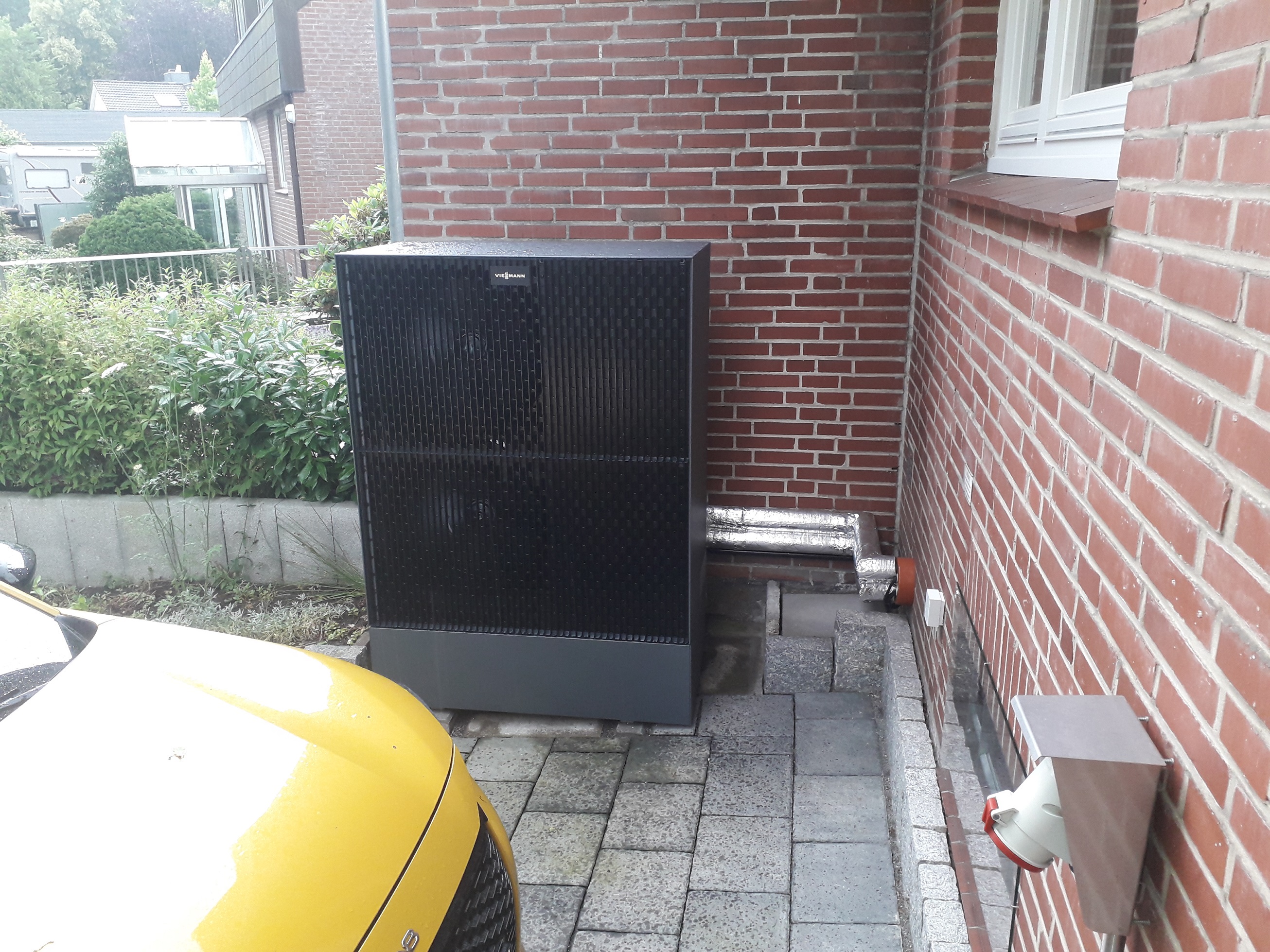 Luft-Wasser Wärmepumpe in der Ecke zwischen dem Haus und dem versetzt liegenden Nachbarhaus